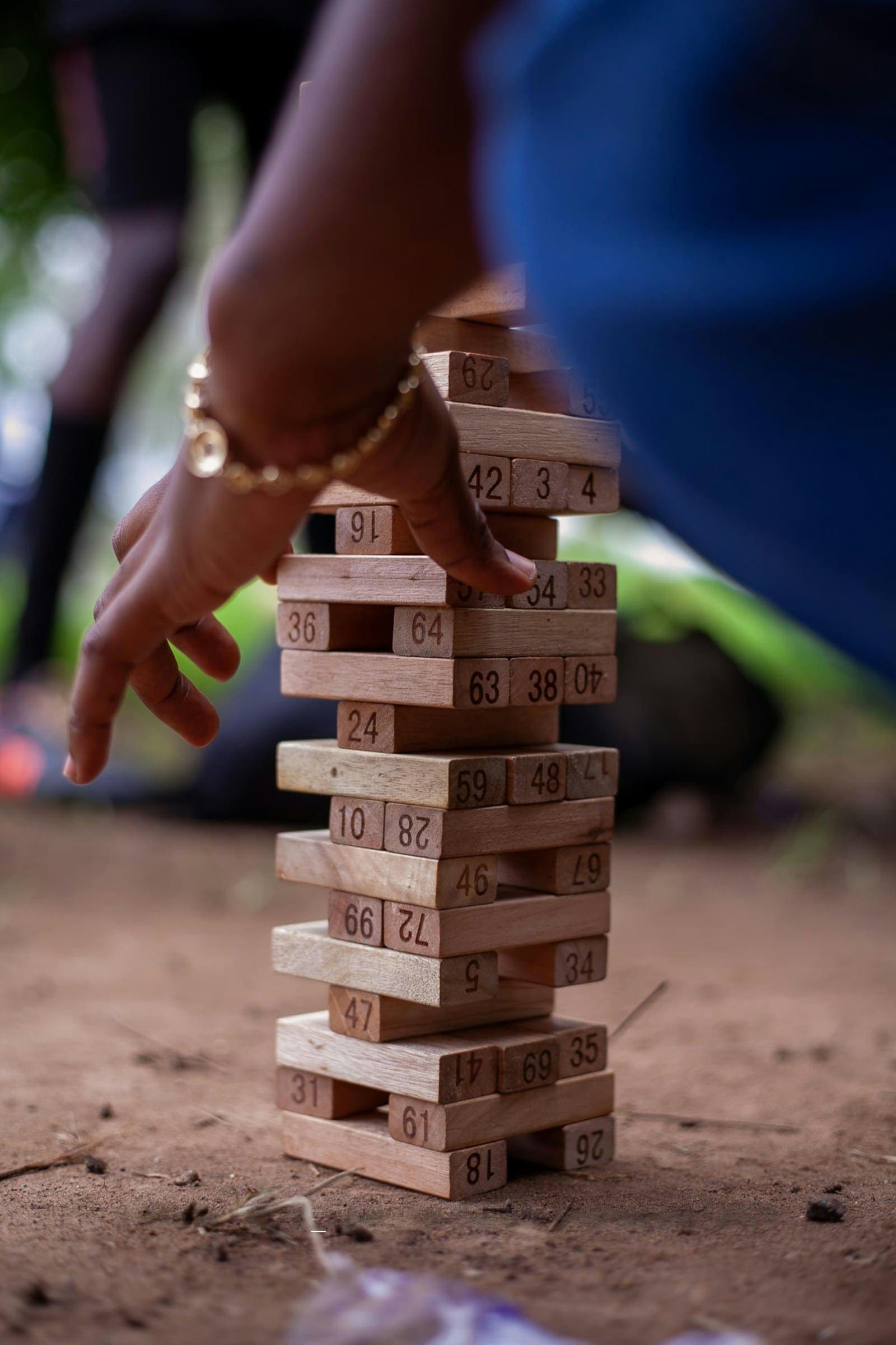 A hand carefully pulling a block from a giant tumbling block tower