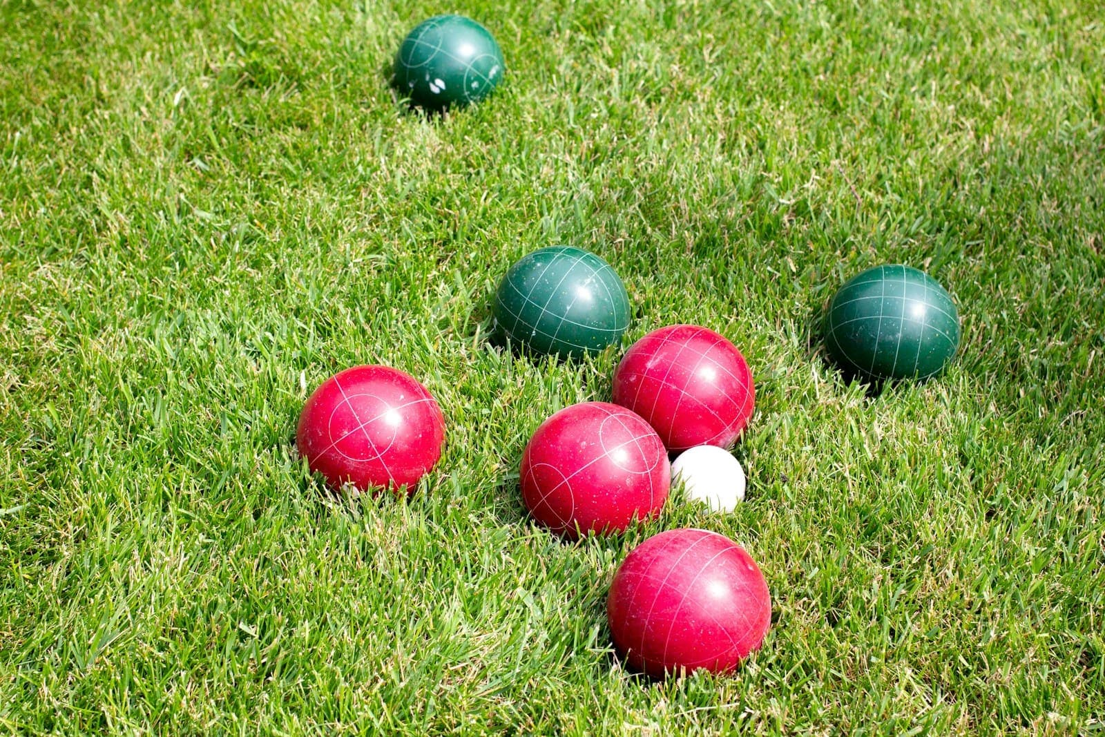 Red and green bocce balls resting on a sunny lawn